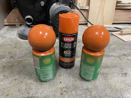 two half painted balls resting on soda cans with a can of krylon gloss popsicle orange in the background